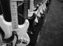 Several electric guitars sit lined up in a row on display with an amplifier in the background.