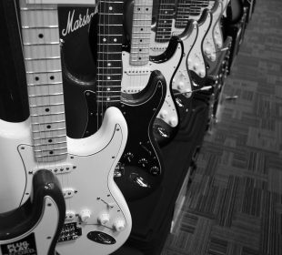 Several electric guitars sit lined up in a row on display with an amplifier in the background.