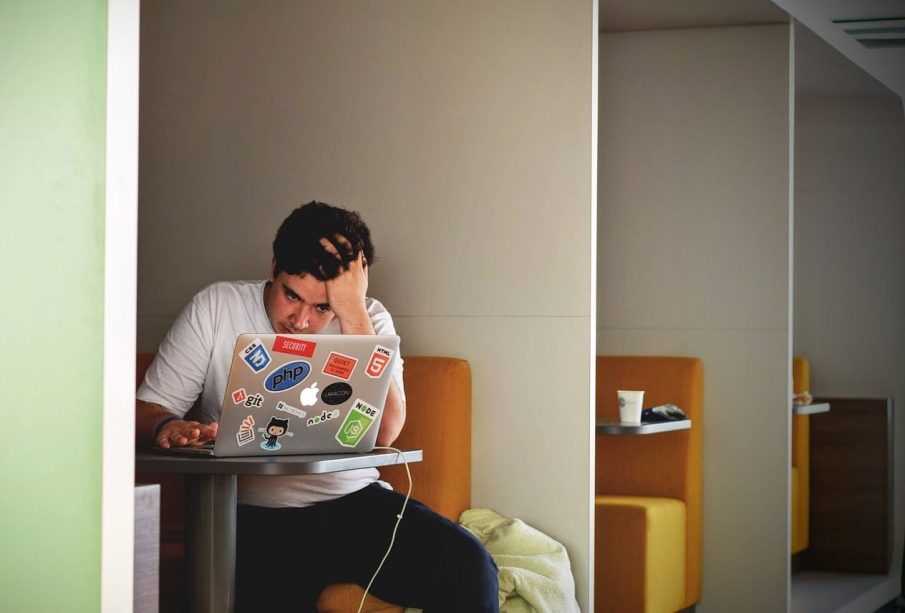 Someone sits in a booth with their head in their hand, staring at their laptop with frustration.