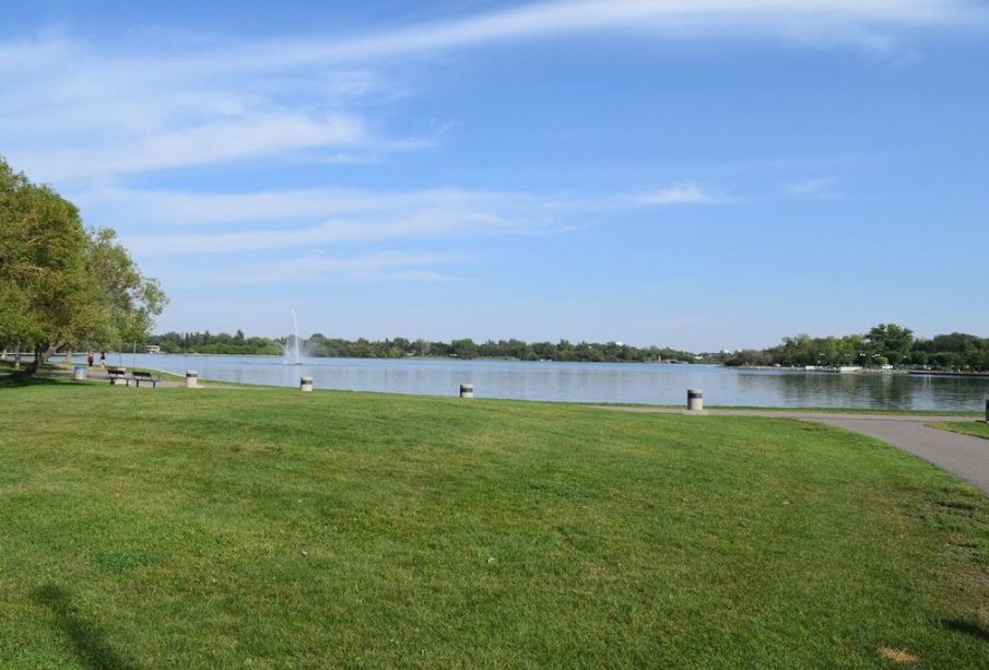 A panoramic shot of Wascana Lake, with green grass and a view of the lake waters.