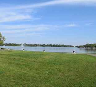 A panoramic shot of Wascana Lake, with green grass and a view of the lake waters.