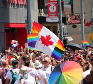 A photo from a pride parade, with a flag merging the flag of Canada and the pride flag in the forefront