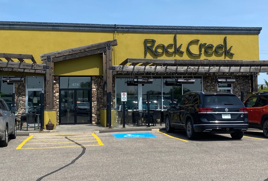 A view from the parking lot of the restaurant Rock Creek. There are three SUVs parked right by the entrance, one that’s grey on the left side with one red and one black on the right.