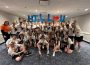 The Hill team poses for a group photo in matching team shirts and lanyards. A few members hold up signs in the back row to spell out “HILL