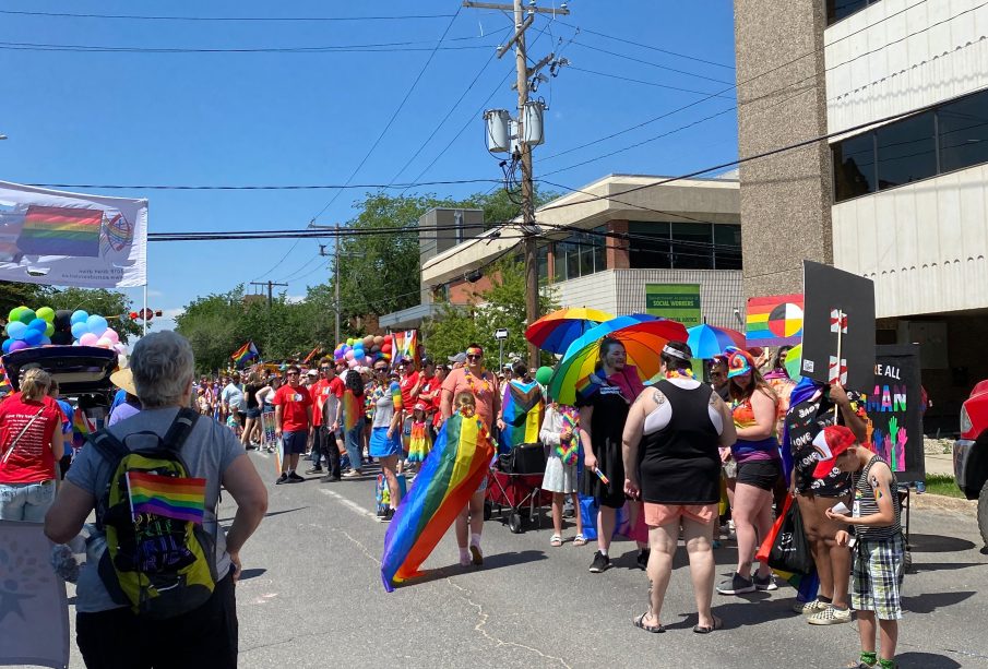 A large group of people clad in Pride flags and surrounded by many more Pride flags participating in the Queen City Pride Parade.