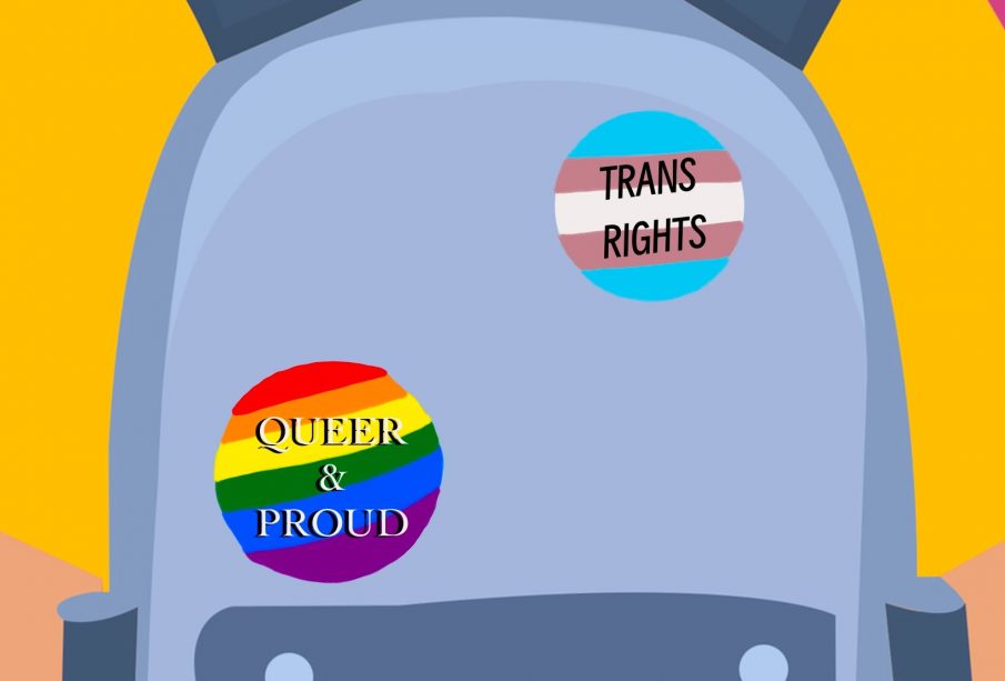 A person in a yellow shirt stands against a pink background. They’re wearing a grey backpack with three pins: one rainbow-striped heart, one rainbow-striped circle with the words “QUEER & PROUD,” and a circle with the colours of the trans flag that says “TRANS RIGHTS.”