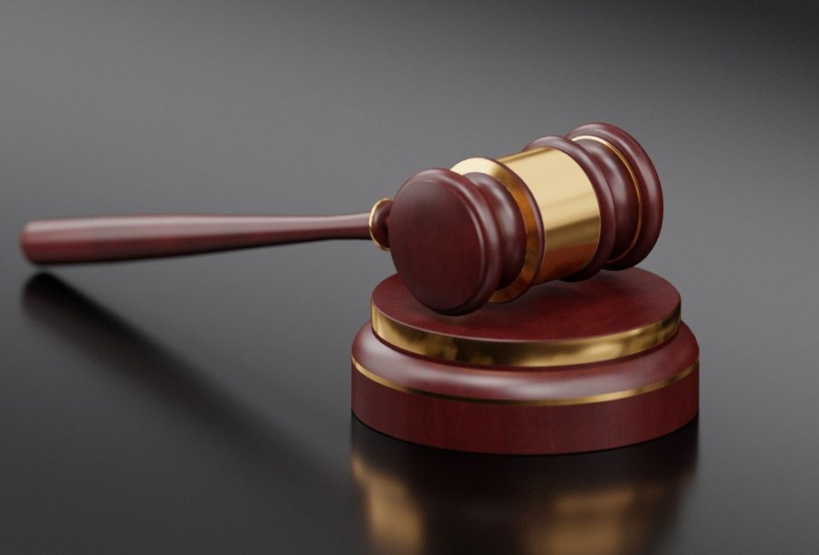 A dark-stained wooden gavel with strips of gold colouring lying on top of a similarly coloured sound block.