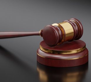 A dark-stained wooden gavel with strips of gold colouring lying on top of a similarly coloured sound block.