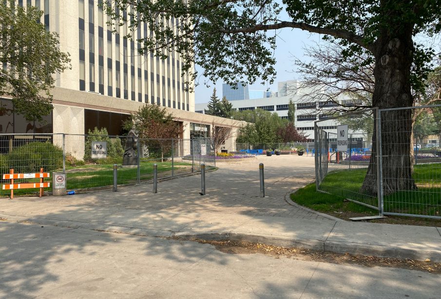 A photo taken from the street to the west of Regina’s city hall which shows the lawn space fully blocked off by fences which have “NO TRESSPASSING” signs attached to them.
