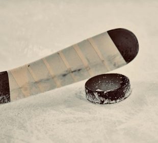 A hockey stick positioned right above a hockey puck.