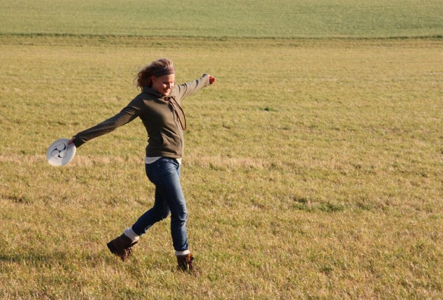 A person standing in an open field, arms stretched. They are holding a Frisbee in one hand.