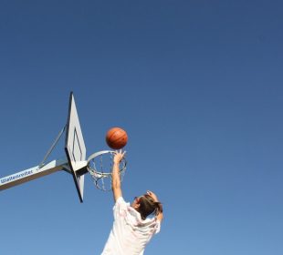 A person jumping towards a basketball hoop, tossing the basketball at an angle that looks like it’ll sink in the hoop no problem