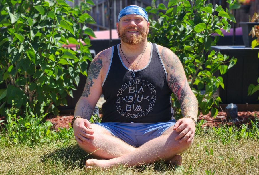 Yoga instructor Sacha Wolfson sits cross-legged outside with his hands on his knees, enjoying the sunshine.