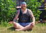 Yoga instructor Sacha Wolfson sits cross-legged outside with his hands on his knees, enjoying the sunshine.
