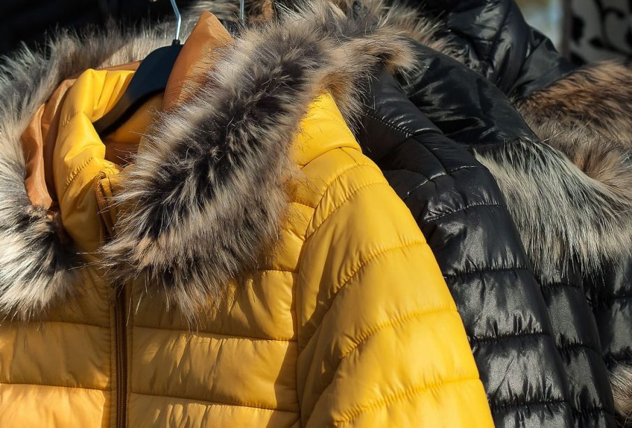 Three black coats and one yellow coat with fur-lined hoods hang on a rack. 