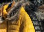 Three black coats and one yellow coat with fur-lined hoods hang on a rack. 