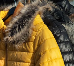 Three black coats and one yellow coat with fur-lined hoods hang on a rack. 