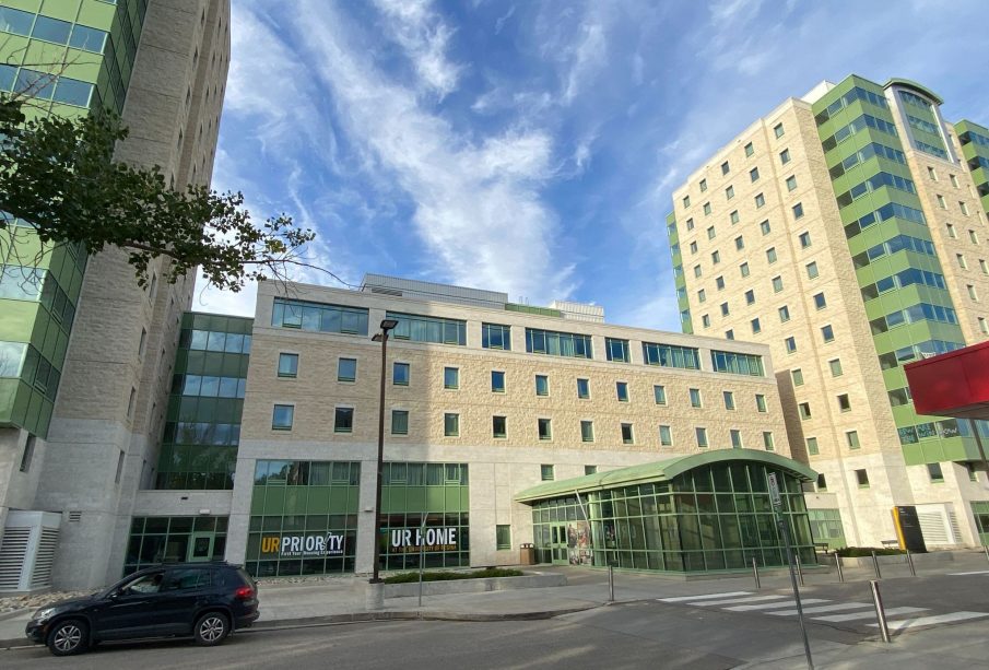 A photo depicts a University of Regina student residence against a dramatic blue, cloud-streaked sky.
