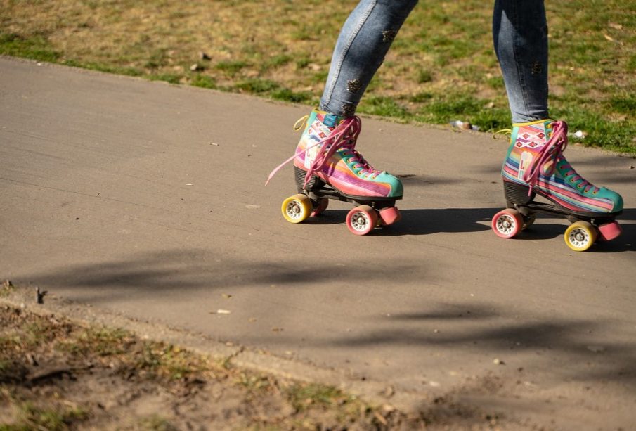 A person wearing multi-coloured roller-skates glides down a walkway bordered by grass.  
