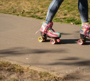 A person wearing multi-coloured roller-skates glides down a walkway bordered by grass.  