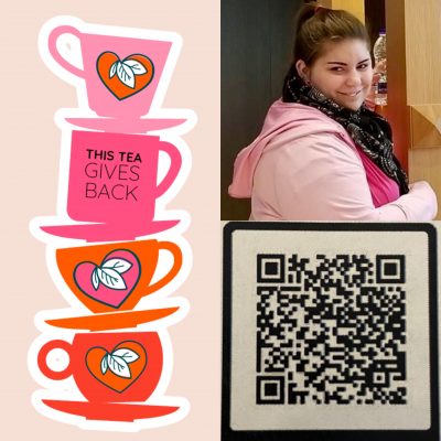 There is a stack of tea cups and plates beside an image of a person. On the left side there are four pink and orange tea cups stacked with their tea plates between them. There are triple leaf designs on three of the tea cups, while the second from the top has “This Tea Gives Back” written on it. The person to the write of the image is wearing black leggings, a light pink sweater, and a hot pink shirt along with a black purse and a black and white patterned scarf. They are smiling to the left of the camera and grabbing a water from a shelf that is behind their head and to their left.