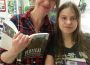 A mother and daughter smile at the camera, both with books in hand.