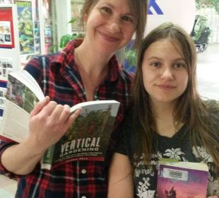 A mother and daughter smile at the camera, both with books in hand.