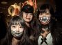 Three people with Halloween themed make-up in a photograph. The one on the left side has drawn a smiling mouth with sharp teeth onto her face, the one in the middle has a zipper opening her cheek under her eye and a scar pulling the side of her mouth open by using liquid latex, and the one on the right has a liquid latex and fake sharp tooth-ed mouth stretching across her face and covering her nose.
