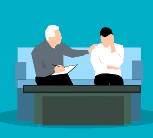 A young adult is sitting on a couch with a counsellor, who has their hand on their shoulder supportively.