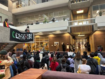 Protestors gather inside to listen to speakers with a “Cease Fire” sign hanging from an upper level.