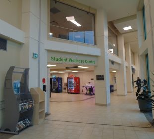A photo of a corridor, with some vending machines visible. A sign says “Student Wellness Centre.”