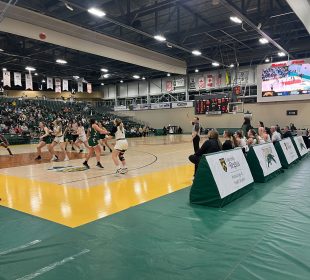 A photo of the University of Regina and Fraser Valley’s women’s basketball teams playing a match. The players are focused on the basketball in the air. The score is 33:25 in Fraser Valley’s favour.