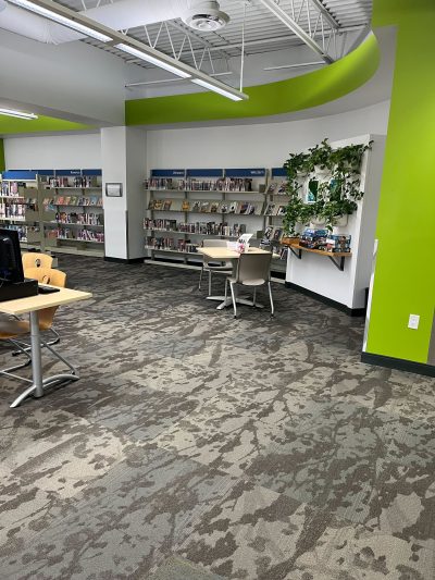 One section of a public library branch, with some desks and chairs. The wall is lined with bookshelves.