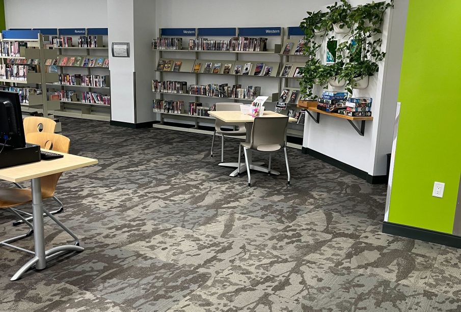 One section of a public library branch, with some desks and chairs. The wall is lined with bookshelves.