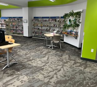One section of a public library branch, with some desks and chairs. The wall is lined with bookshelves.
