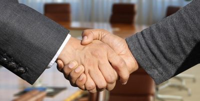 A handshake between two masculine-appearing hands, one showing a suit coat cuff and the other a casual sweater cuff.