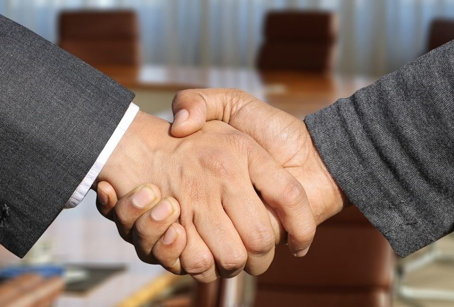 A handshake between two masculine-appearing hands, one showing a suit coat cuff and the other a casual sweater cuff.
