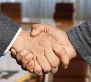 A handshake between two masculine-appearing hands, one showing a suit coat cuff and the other a casual sweater cuff.