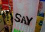 A photograph of a massive banner filled with handwritten names of roughly 5,000 of the murdered in Palestine drapes from the second story and across the lower-level floor titled “Say Their Names.”