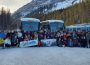 A group photo of students in Banff on the ski and board trip, posing in front of their charter buses and a tree-covered mountain. 