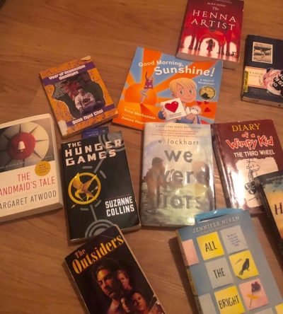 This photo shows a spread of books laid out on the floor. These books range from children’s books, all the way to young adult novels. Some of the classics listed include Diary of A wimpy Kid, The Hunger Games, and The Handmaid’s Tale.