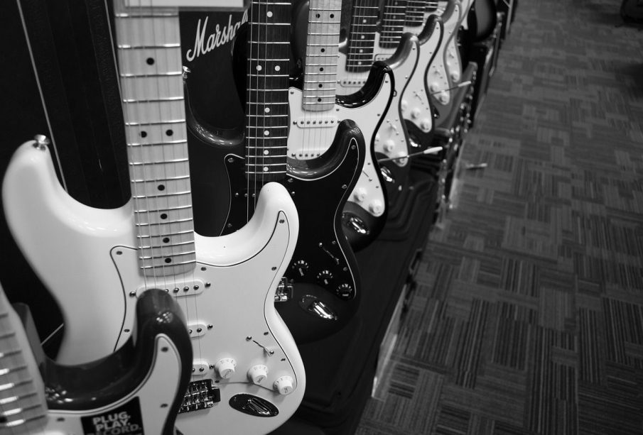 Several electric guitars sit lined up in a row on display with an amplifier in the background.