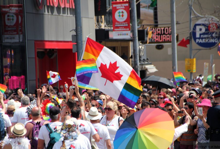 A photo from a pride parade, with a flag merging the flag of Canada and the pride flag in the forefront