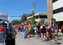 A large group of people clad in Pride flags and surrounded by many more Pride flags participating in the Queen City Pride Parade.