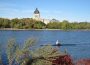 A person rowing a boat on Wascana lake on a sunny day. The Legislative Building is visible in the background.