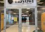 A photo of the double doors to the Lazy Owl at the University of Regina. The doors are made of glass and stainless steel. Above the doors there is a white banner containing a line art image of an owl in a shield and “LazyOwl” in bold, black lettering. Beneath the lettering is “EST. 1967” and the Lazy Owl’s website link: lazyowlyqr.ca.