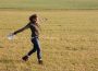 A person standing in an open field, arms stretched. They are holding a Frisbee in one hand.