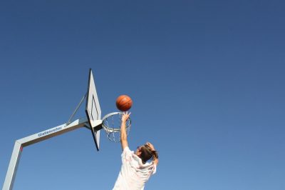 A person jumping towards a basketball hoop, tossing the basketball at an angle that looks like it’ll sink in the hoop no problem