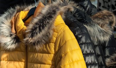 Three black coats and one yellow coat with fur-lined hoods hang on a rack. 