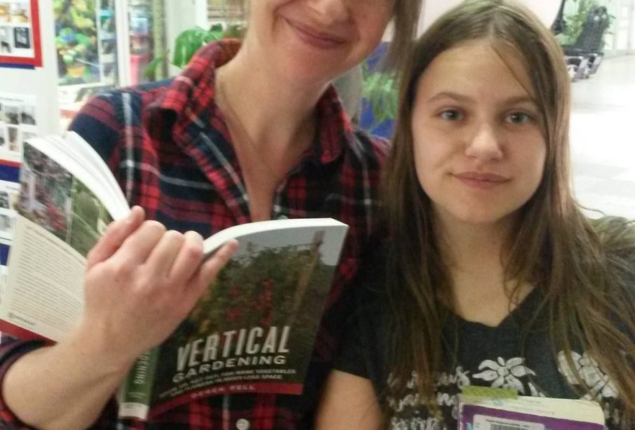 A mother and daughter smile at the camera, both with books in hand.